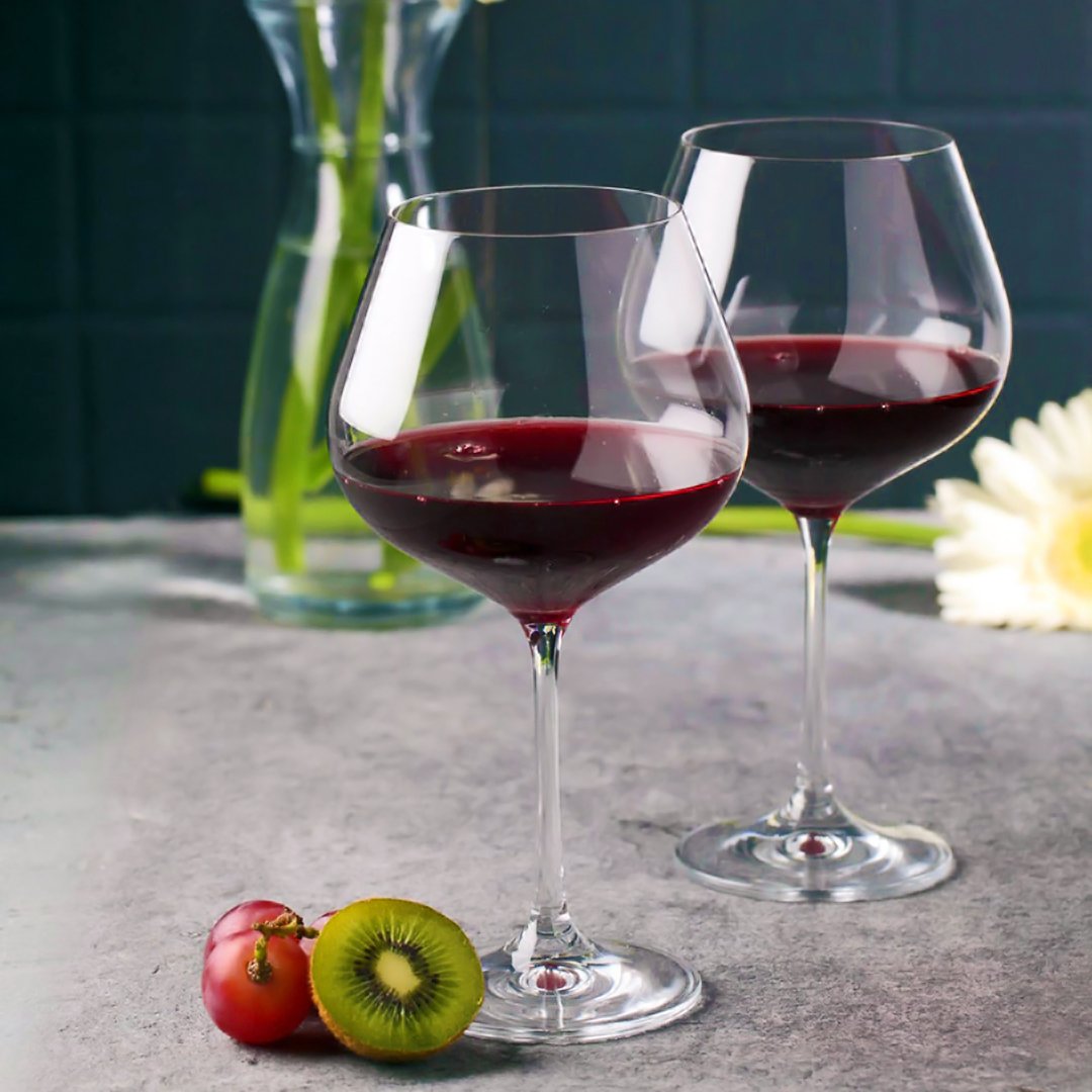 Crystal clear wine glass filled with rich red wine against a backdrop of vineyard leaves and grapes.