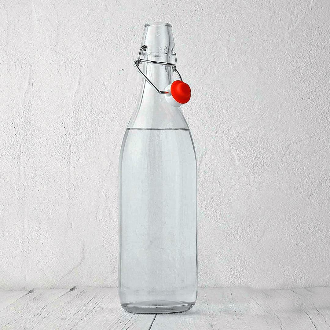 Flip top glass water bottle filled with water on a desk.